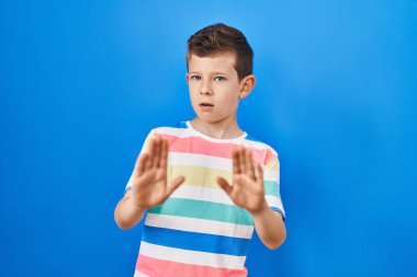 Mavi arka plan üzerinde duran beyaz bir çocuk. Avuçlarını hareket ettiriyor. Korkmuş ve iğrenç bir ifadeyle reddediyor. Dur ve yasakla. 