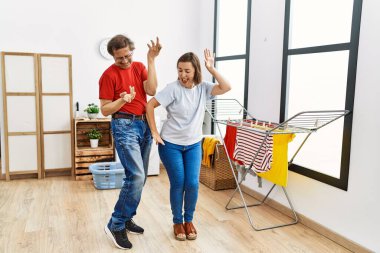 Orta yaşlı erkek ve kadın çamaşırhanede çamaşır makinesini beklerken dans ediyorlar.