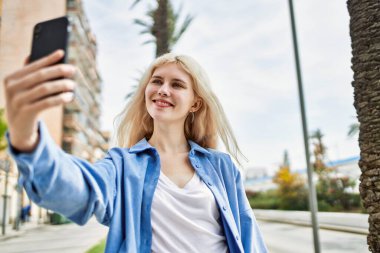 Genç sarışın kadın güneşli bir günde akıllı telefonuyla selfie çekiyor.