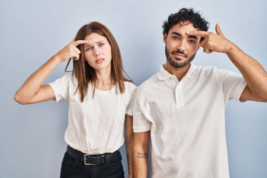 Young couple wearing casual clothes standing together pointing unhappy to pimple on forehead, ugly infection of blackhead. acne and skin problem 