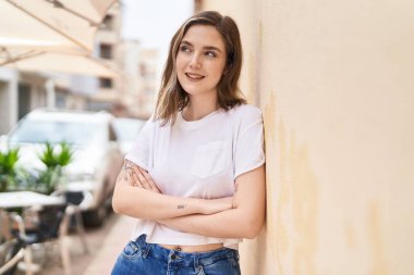 Kendine güvenen genç bir kadın caddede kollarını kavuşturmuş duruyor.