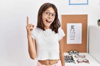 Young hispanic girl wearing glasses pointing finger up with successful idea. exited and happy. number one. 
