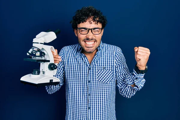 Young Hispanic Man Holding Microscope Screaming Proud Celebrating Victory Success — Fotografia de Stock