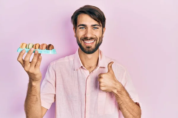 Young Hispanic Man Holding Delicious Macrons Pastries Smiling Happy Positive — Stock Photo, Image