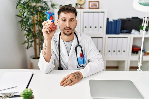 Young Doctor Holding Heart Medical Clinic Thinking Attitude Sober Expression — Foto Stock