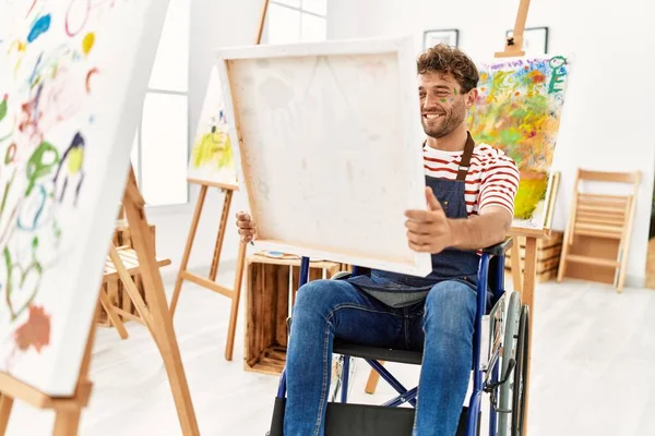 年轻的惊慌失措的男人坐在轮椅上 拿着帆布在艺术工作室里 — 图库照片