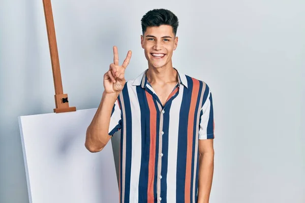 Young Hispanic Man Standing Close Empty Canvas Showing Pointing Fingers —  Fotos de Stock