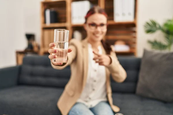 Молода Біла Жінка Пропонує Склянку Води Посміхаючись Щасливий Вказуючи Рукою — стокове фото