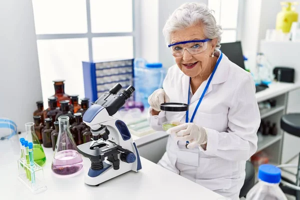 研究室でループを使って科学者の制服を着たシニア白髪の女性 — ストック写真