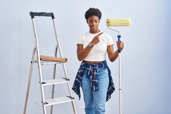 African American Woman Holding Roller Painter Pointing Hand Finger Side — Foto Stock