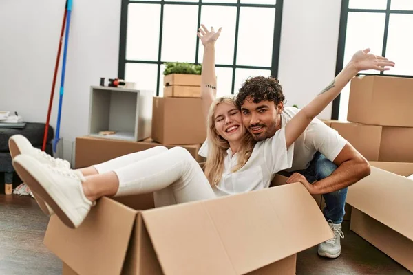 Young beautiful couple smiling happy playing using cardboard box as a car at new home.