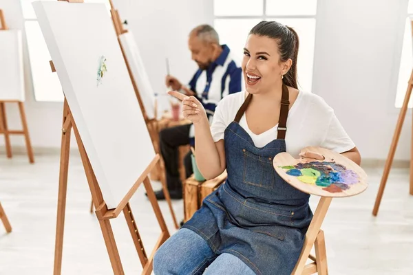 Young artist woman at art studio smiling happy pointing with hand and finger to the side