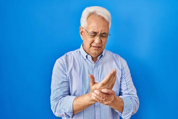 Hispanic senior man wearing glasses suffering pain on hands and fingers, arthritis inflammation