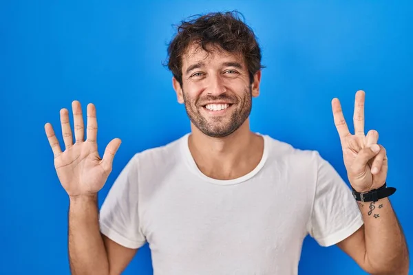 西班牙裔年轻人站在蓝色的背景上 用七号手指指指着 面带微笑 自信而快乐 — 图库照片