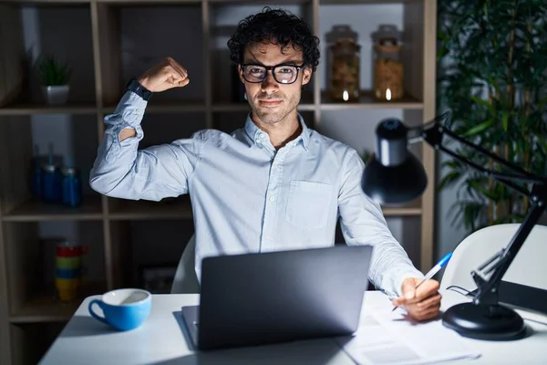 Hispanic man working at the office at night strong person showing arm muscle, confident and proud of power