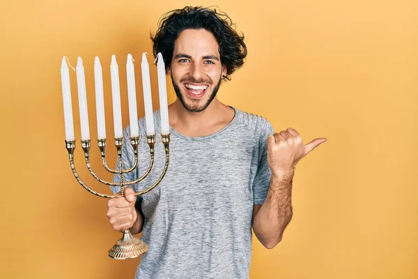 Hombre Hispano Guapo Sosteniendo Menorah Hanukkah Vela Judía Señalando Pulgar —  Fotos de Stock