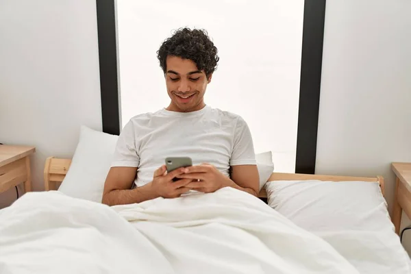 Junger Hispanischer Mann Sitzt Mit Smartphone Schlafzimmer Auf Dem Bett — Stockfoto
