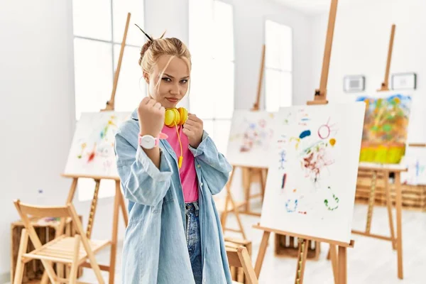 Young caucasian girl at art studio ready to fight with fist defense gesture, angry and upset face, afraid of problem