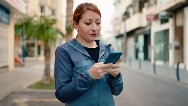 在街上用智能手机穿运动服的红头发年轻女人 — 图库照片