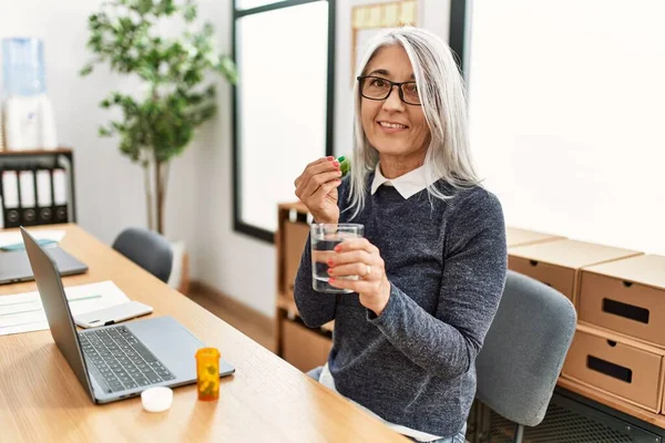 オフィスで働く丸薬を飲んでいる中年の白髪の女性ビジネスワーカー — ストック写真
