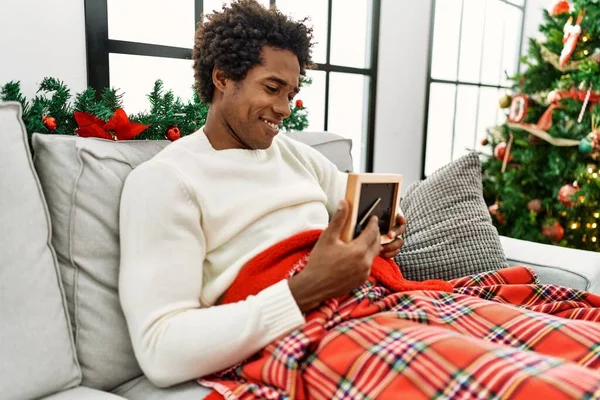 Young African American Man Holding Photo Sitting Sofa Christmas Tree — Stockfoto