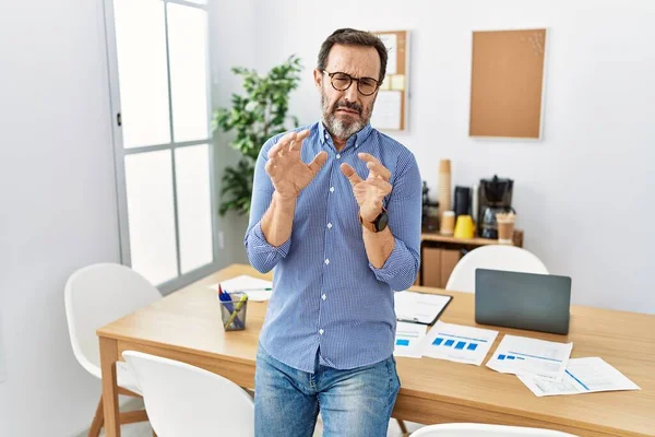 Middle age hispanic man with beard wearing business clothes at the office disgusted expression, displeased and fearful doing disgust face because aversion reaction. with hands raised