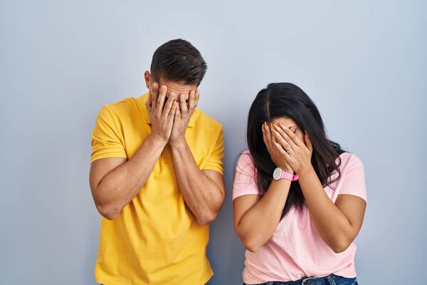 Молодая пара, стоящая на изолированном фоне с грустным выражением лица, закрывая лицо руками во время плача. депрессия. 