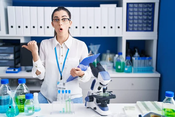 Young Brunette Woman Working Scientist Laboratory Surprised Pointing Hand Finger — ストック写真