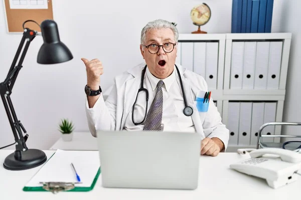 Senior Caucasian Man Wearing Doctor Uniform Stethoscope Clinic Surprised Pointing — Stockfoto