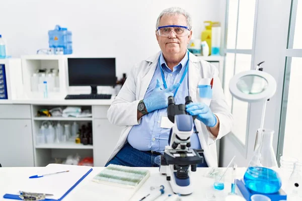 Senior caucasian man working at scientist laboratory cheerful with a smile on face pointing with hand and finger up to the side with happy and natural expression