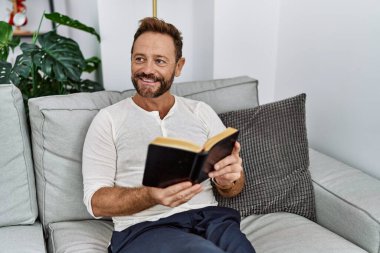 Middle age hispanic man smiling confident reading book at home