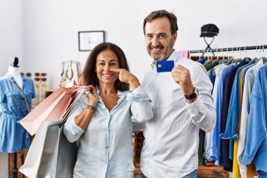 Hispanic middle age couple holding shopping bags and credit card pointing with hand finger to face and nose, smiling cheerful. beauty concept 