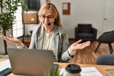 Orta yaş çağrı merkezi ajanının ofisteki bilgisayarı kullanarak görüntülü arama yapması..