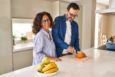 Orta yaşlı İspanyol çift gülümsüyor. Mutfakta turuncu kesiyorlar.