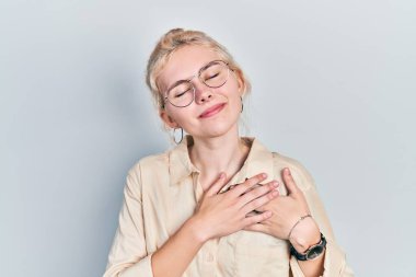 Beautiful caucasian woman with blond hair wearing casual look and glasses smiling with hands on chest with closed eyes and grateful gesture on face. health concept. 