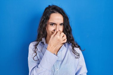 Genç esmer kadın mavi arka planda duruyor. Kokuşmuş ve iğrenç bir koku alıyor. Dayanılmaz bir koku. Kötü kokuyor. 