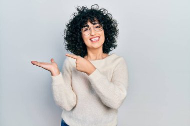 Young middle east woman wearing casual white tshirt amazed and smiling to the camera while presenting with hand and pointing with finger. 
