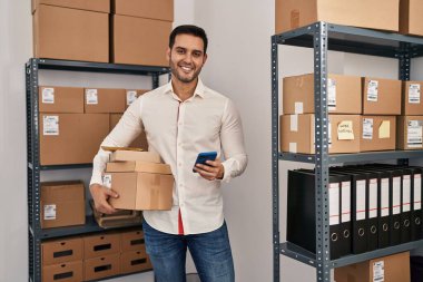 Genç İspanyol bir e-ticaret işçisi ofisteki akıllı telefon paketlerini kullanıyor.