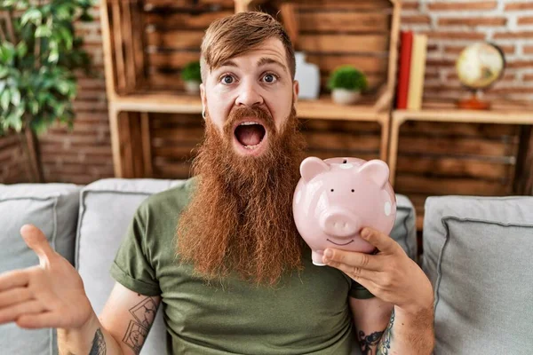 Redhead Man Holding Piggy Bank Celebrating Achievement Happy Smile Winner — Stockfoto