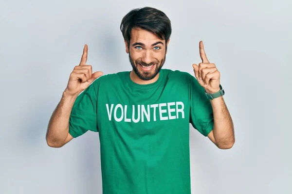 Jovem Hispânico Homem Vestindo Voluntário Shirt Sorrindo Espantado Surpreso Apontando — Fotografia de Stock