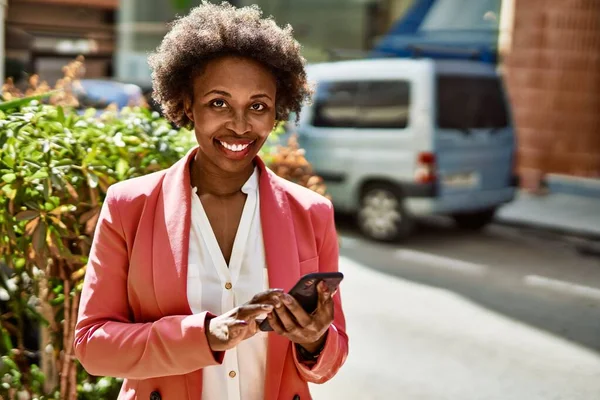 Beautiful business african american woman with afro hair smiling happy and confident outdoors at the city using smarpthone