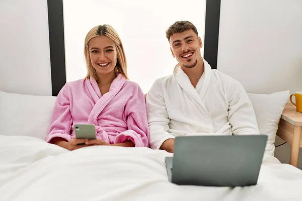 Jovem Casal Caucasiano Sorrindo Feliz Usando Laptop Smartphone Sentado Cama — Fotografia de Stock