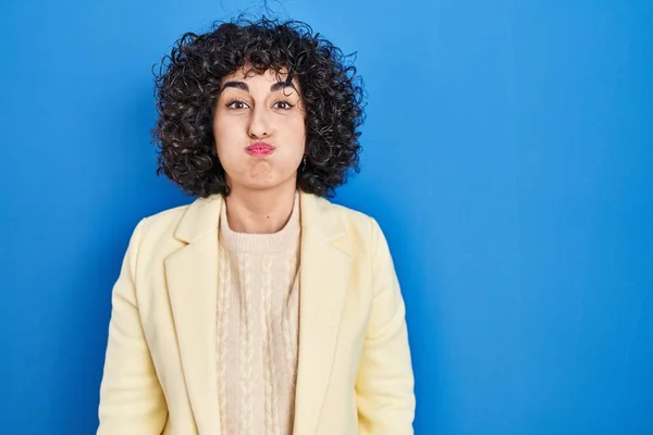 Young Brunette Woman Curly Hair Standing Blue Background Puffing Cheeks — ストック写真