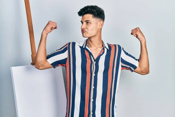 Young Hispanic Man Standing Close Empty Canvas Showing Arms Muscles — Fotografia de Stock