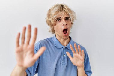 Soyutlanmış arka planda duran genç modern adam korku ifadesinden korkuyor ve dehşete düşüyor. El hareketlerini durdur, şok içinde bağır. panik konsepti. 