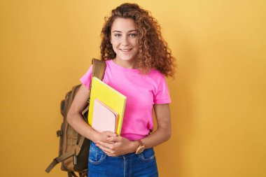 Sırt çantası takan, elinde mutlu ve havalı bir gülümsemeyle kitap tutan beyaz bir kadın. şanslı kişi. 