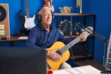 Senior grey-haired man musician singing song playing guitar at music studio