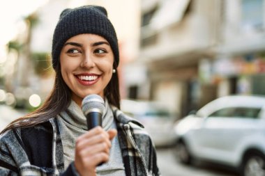 Genç İspanyol kadın şehirde mikrofon kullanarak mutlu bir şekilde gülümsüyor..