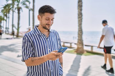 Genç yakışıklı adam deniz kenarında akıllı telefon kullanıyor.