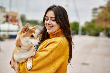 Güzel genç bir kadın sokakta mutlu Shiba Inu köpeğine sarılıyor.